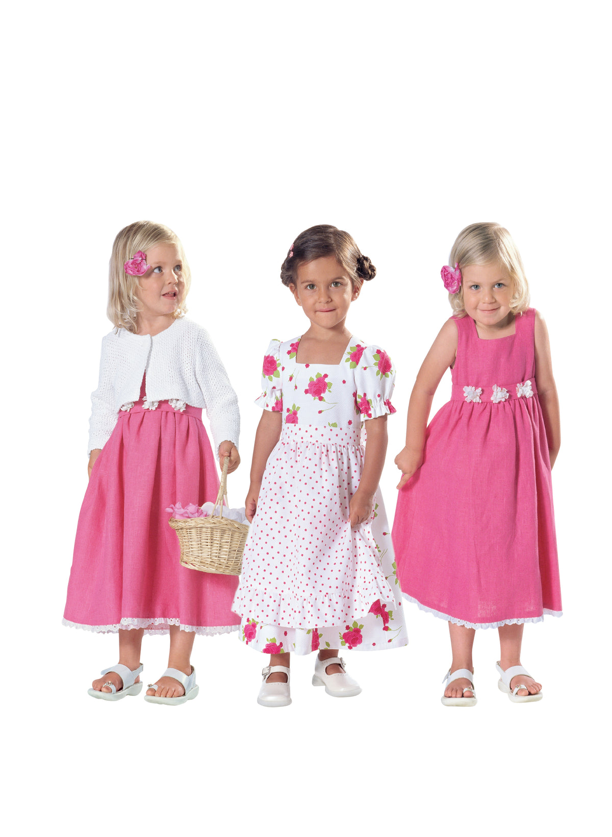 Trois petites filles en robes estivales roses et blancs, l’une tenant un panier, prêtes pour une fête.