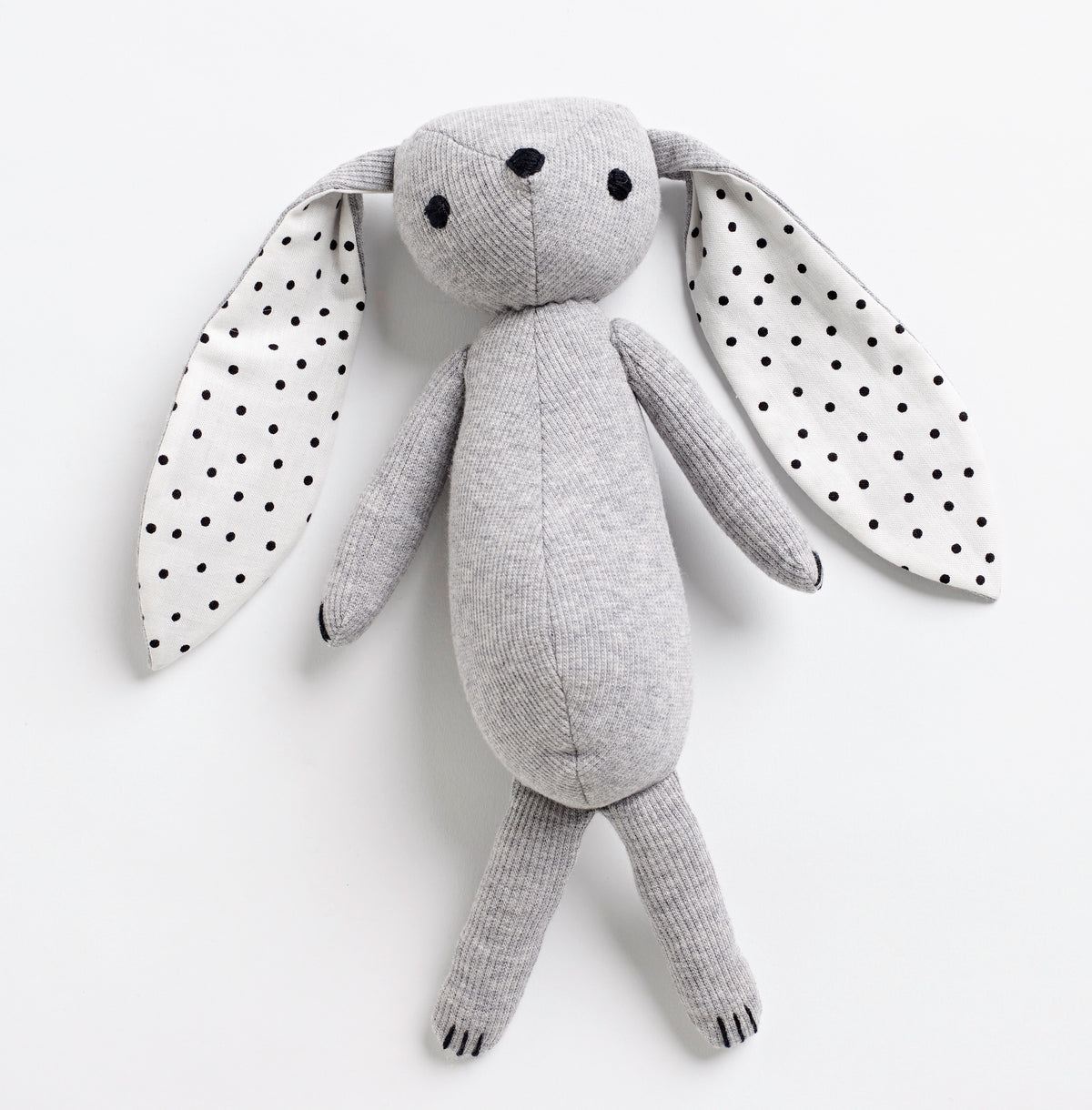 Peluche grey en forme de lapin avec grandes oreilles intérieures à pois noirs, corps allongé et mini pattes.