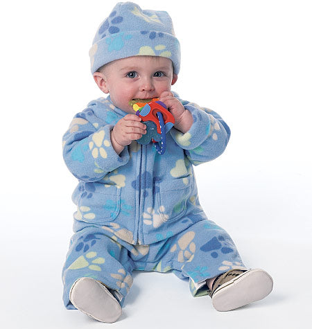 Petit enfant en grenouillère et bonnet bleus à motifs, assis, tenant un jouet coloré.