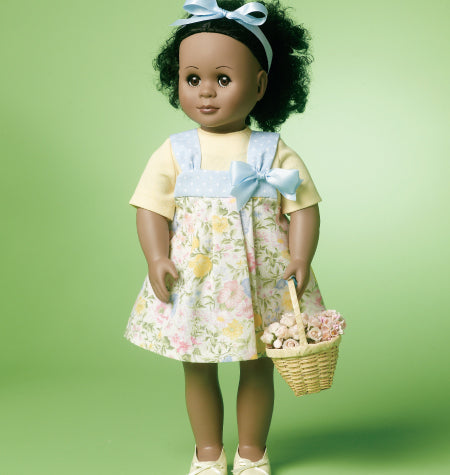 Poupée noire portant robe à motifs fleurs pastel et bavoir bleu, avec panier de fleurs et ruban bleu sur fond vert.